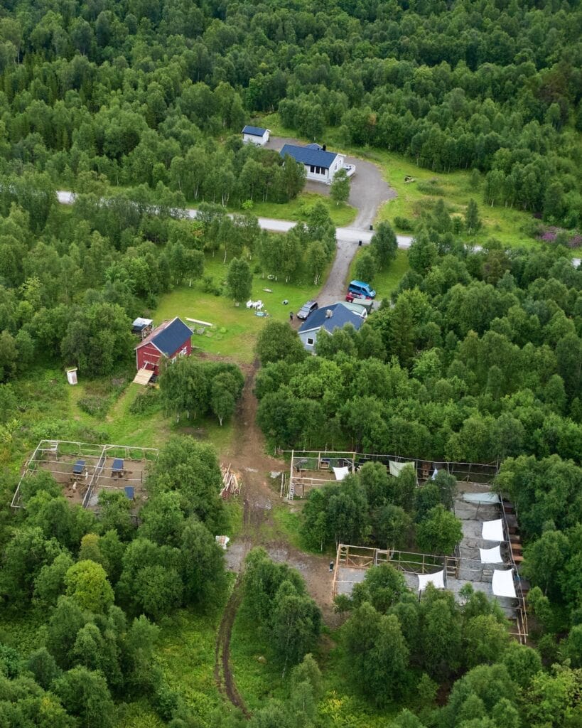 Luftaufnahme der Huskyfarm mit rotem Haus, Hundegehegen und Birkenwald