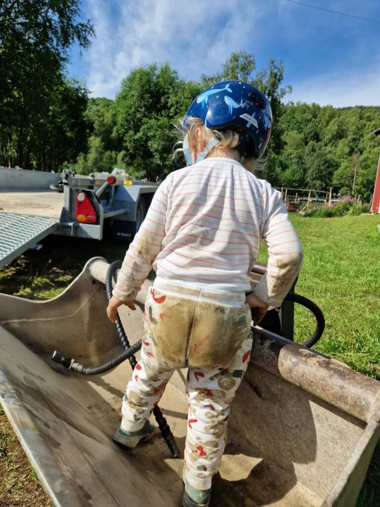 Ein Kind mit Fahrradhelm steht in der Schubkarre beim Sandtransport für die Zwinger